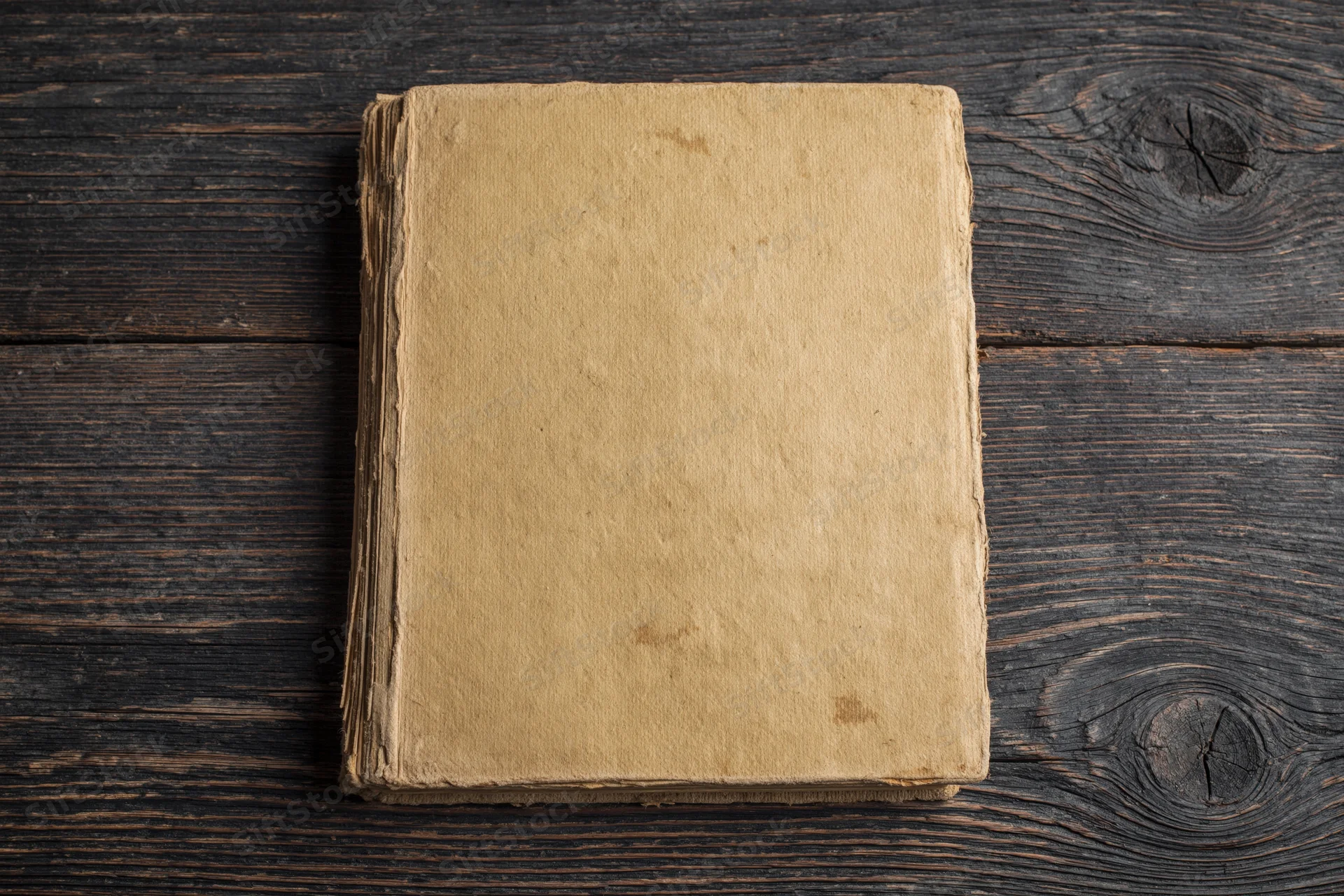 Worn antique book lying face-up on dark weathered wooden surface