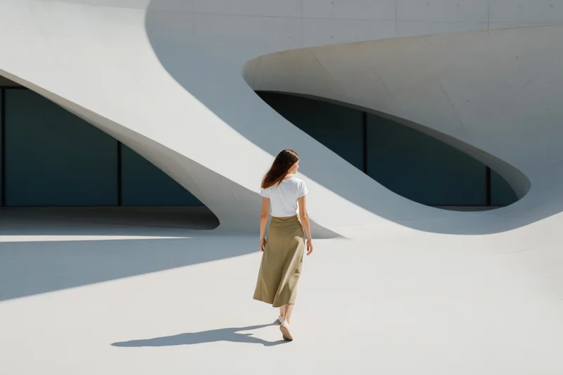 Woman walking away from camera through dramatic curved white architectural structure in daylight
