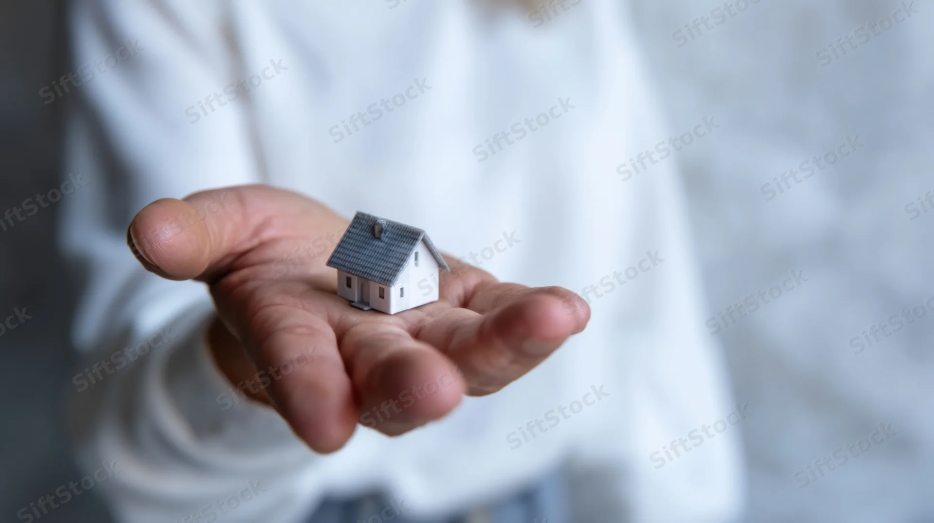 Hand holding a miniature house model against a soft blurred background