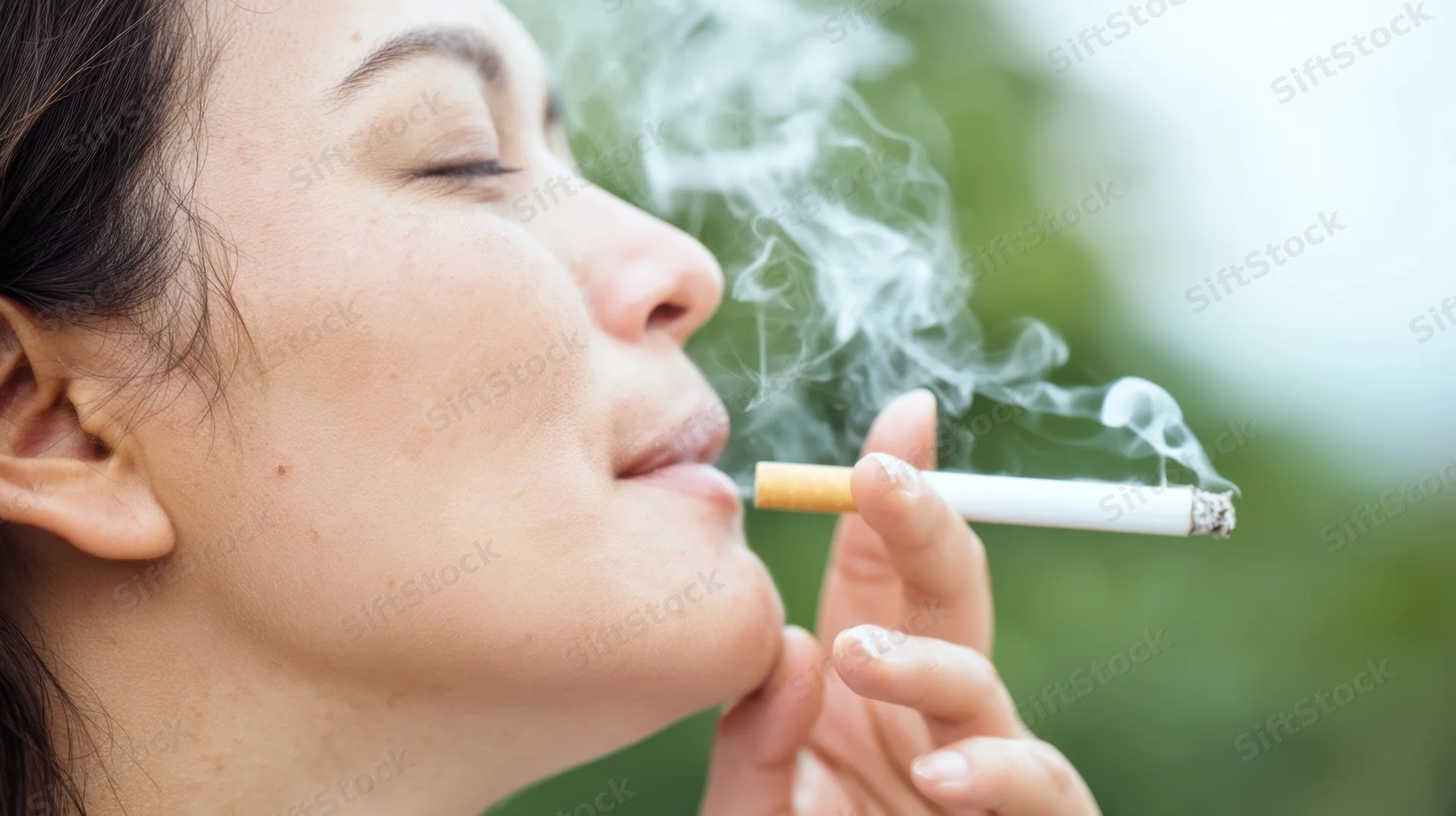 Woman in side profile smoking a cigarette outdoors with smoke rising from the lit end