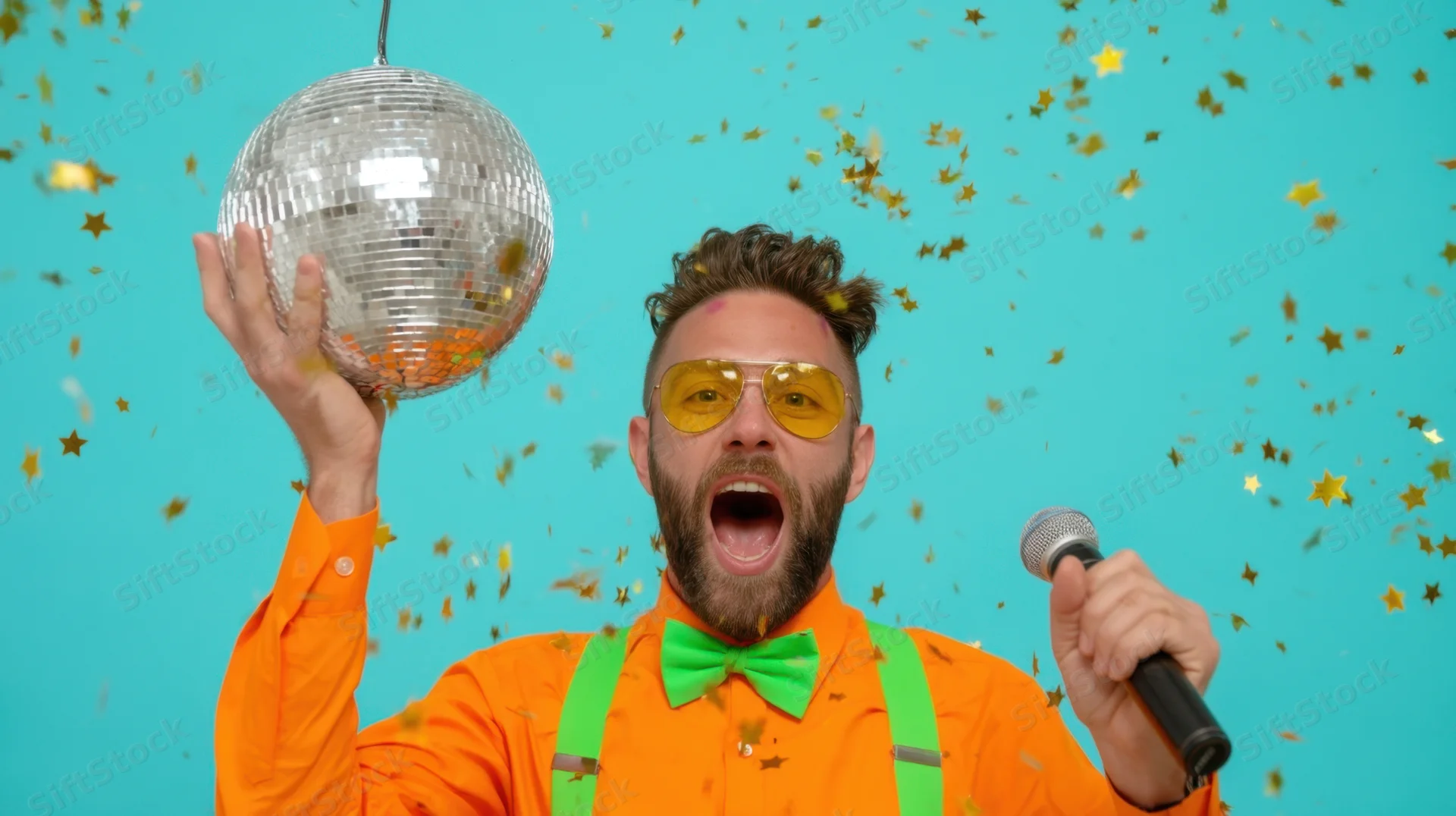 Man singing into microphone while holding disco ball amidst falling confetti against blue background