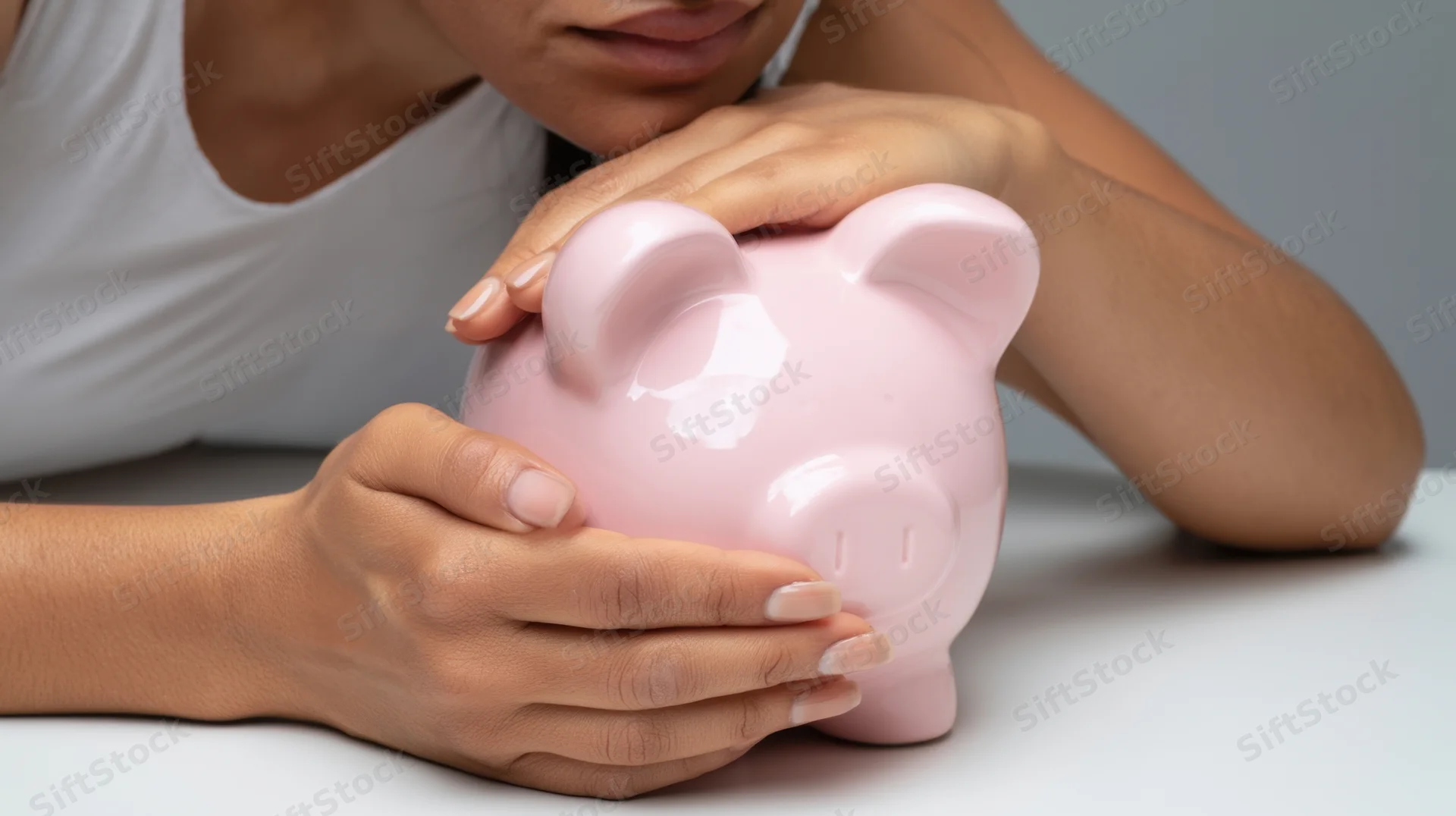 Woman holding pink piggybank on white surface