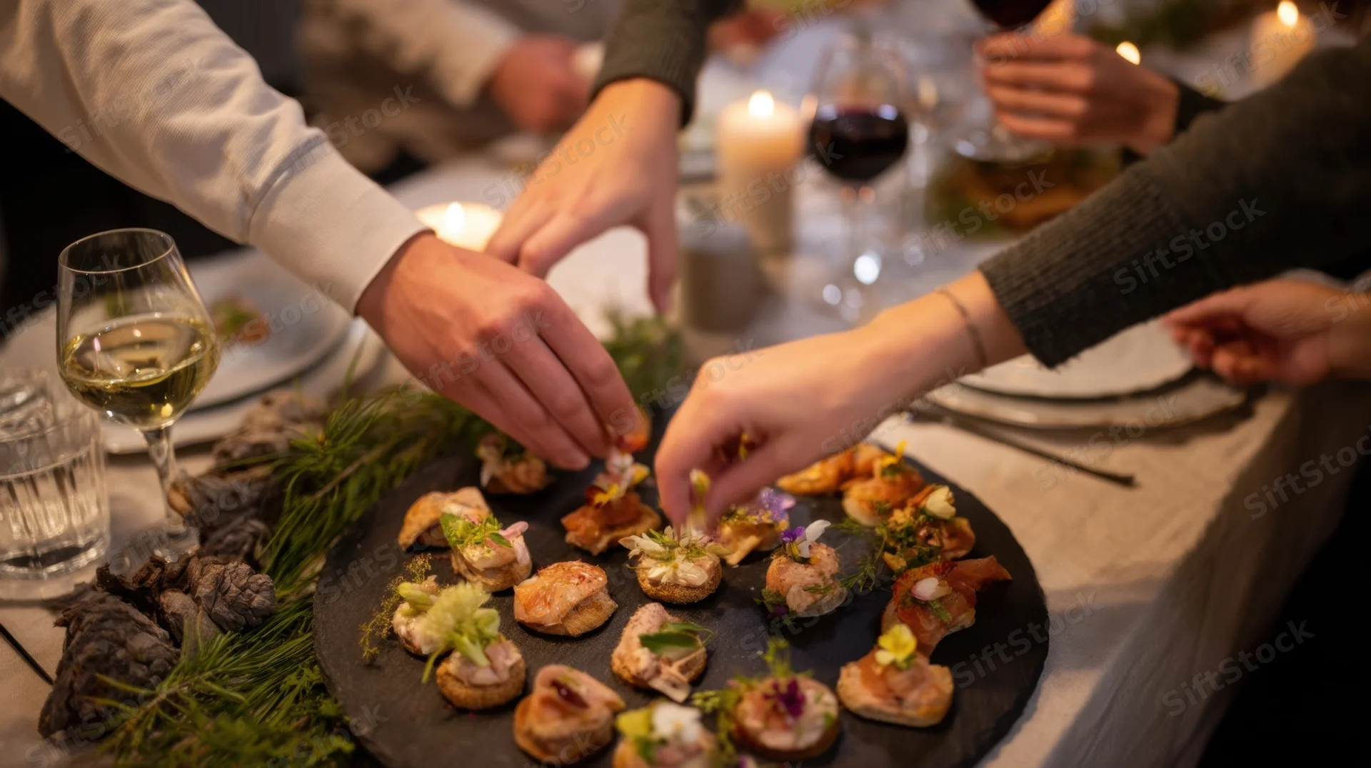 Hands serving gourmet canapes on a slate platter at a candlelit dinner table
