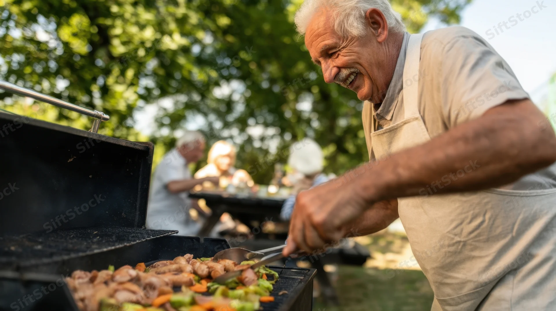 Senior man grilling vegetables and meat on a barbecue in a backyard garden with family in the background