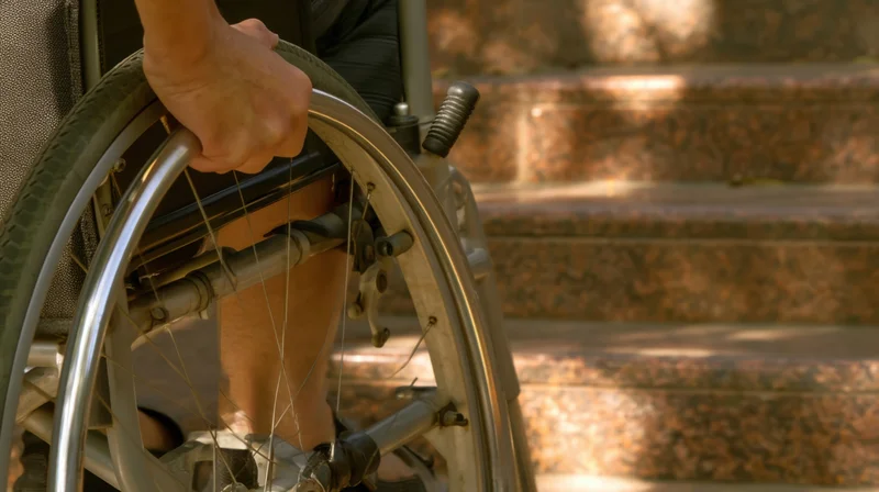 Man in wheelchair gripping wheel near stone steps outdoors