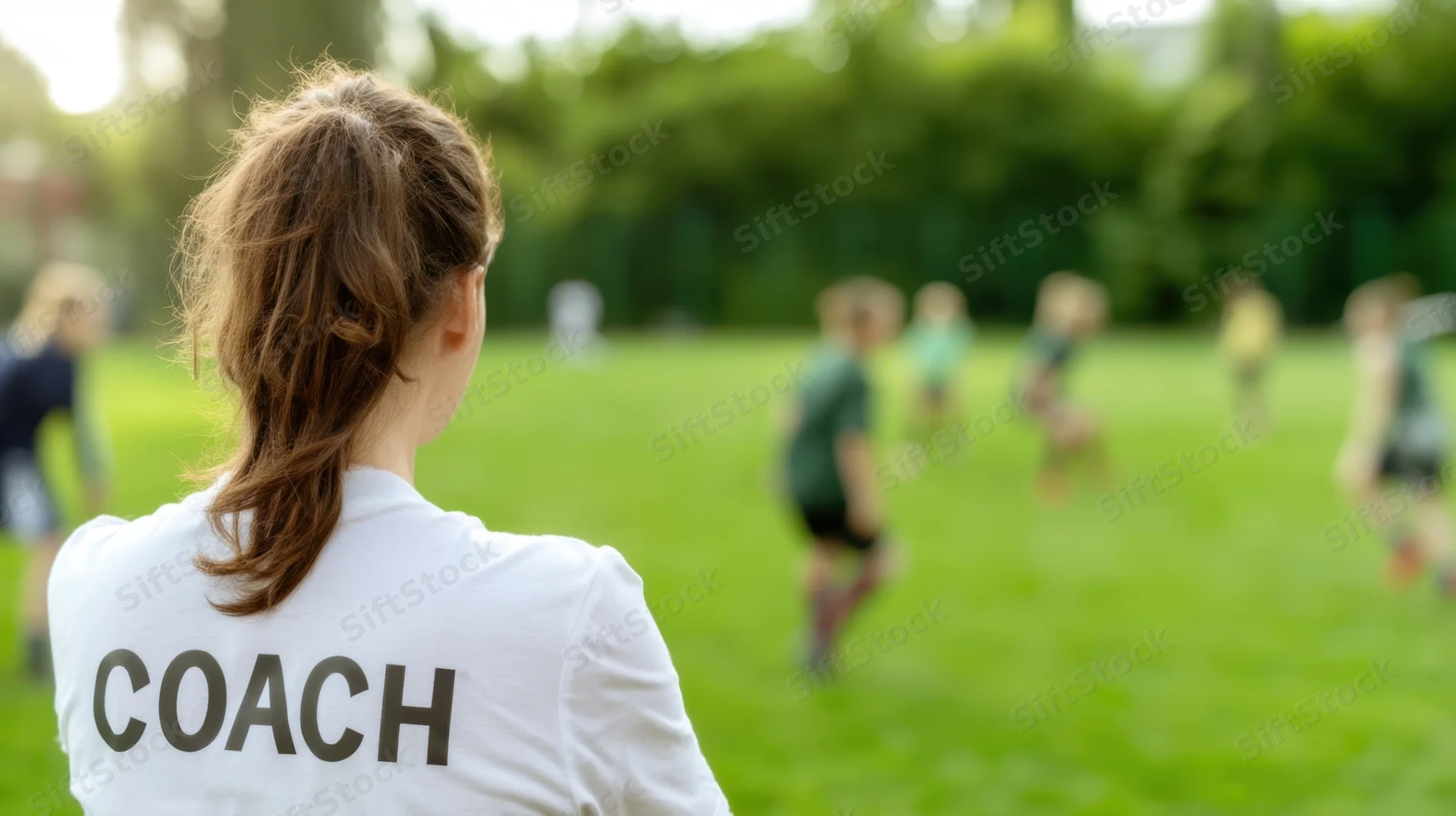 Woman coach watching children play soccer on a grass field