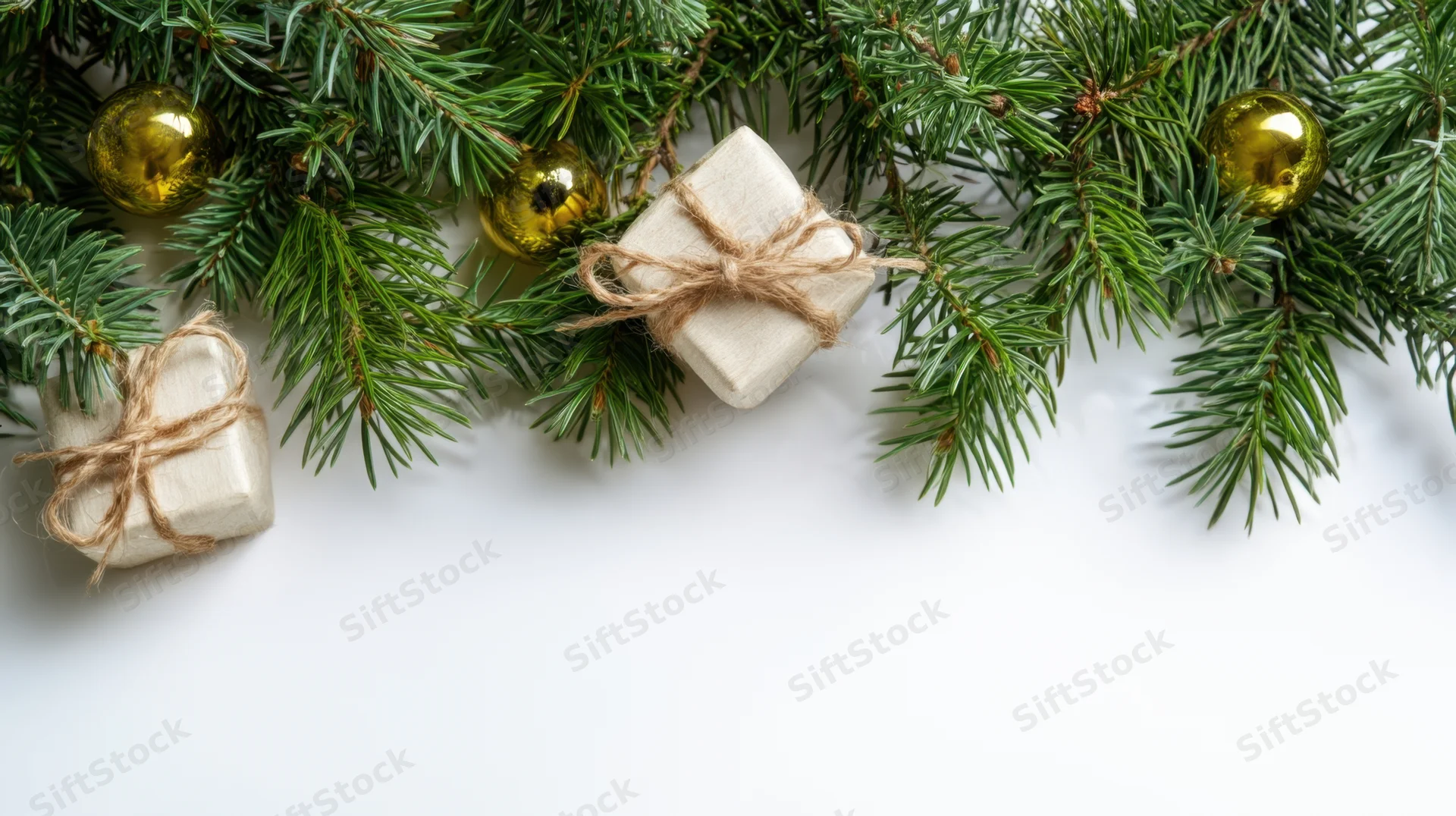 Evergreen garland with gold ornaments and wrapped gifts arranged along the top of a white surface