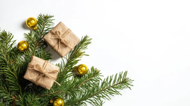 Evergreen branches with wrapped gifts and gold ornaments arranged on white surface
