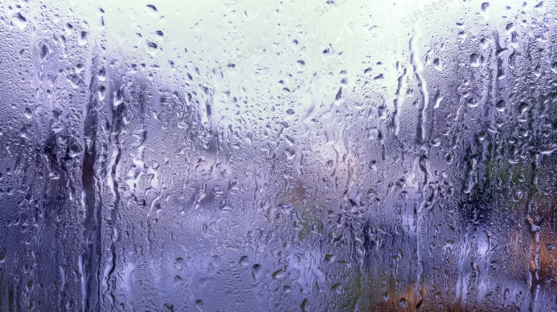 Raindrops streaming down a foggy glass window with blurred outdoor view