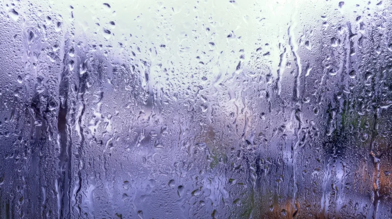 Raindrops streaming down a foggy glass window with blurred outdoor view
