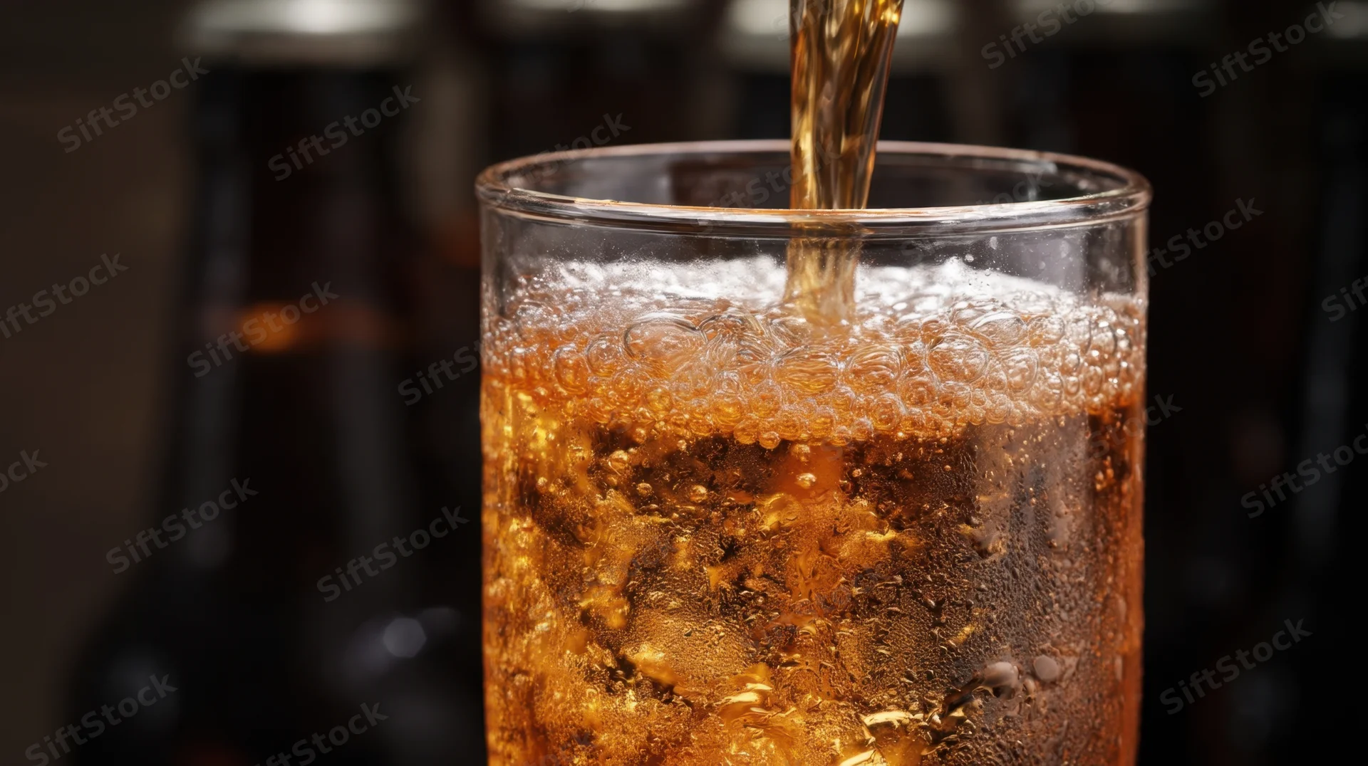 Amber beer pouring into a glass with bubbles and condensation, set against dark bottles in background