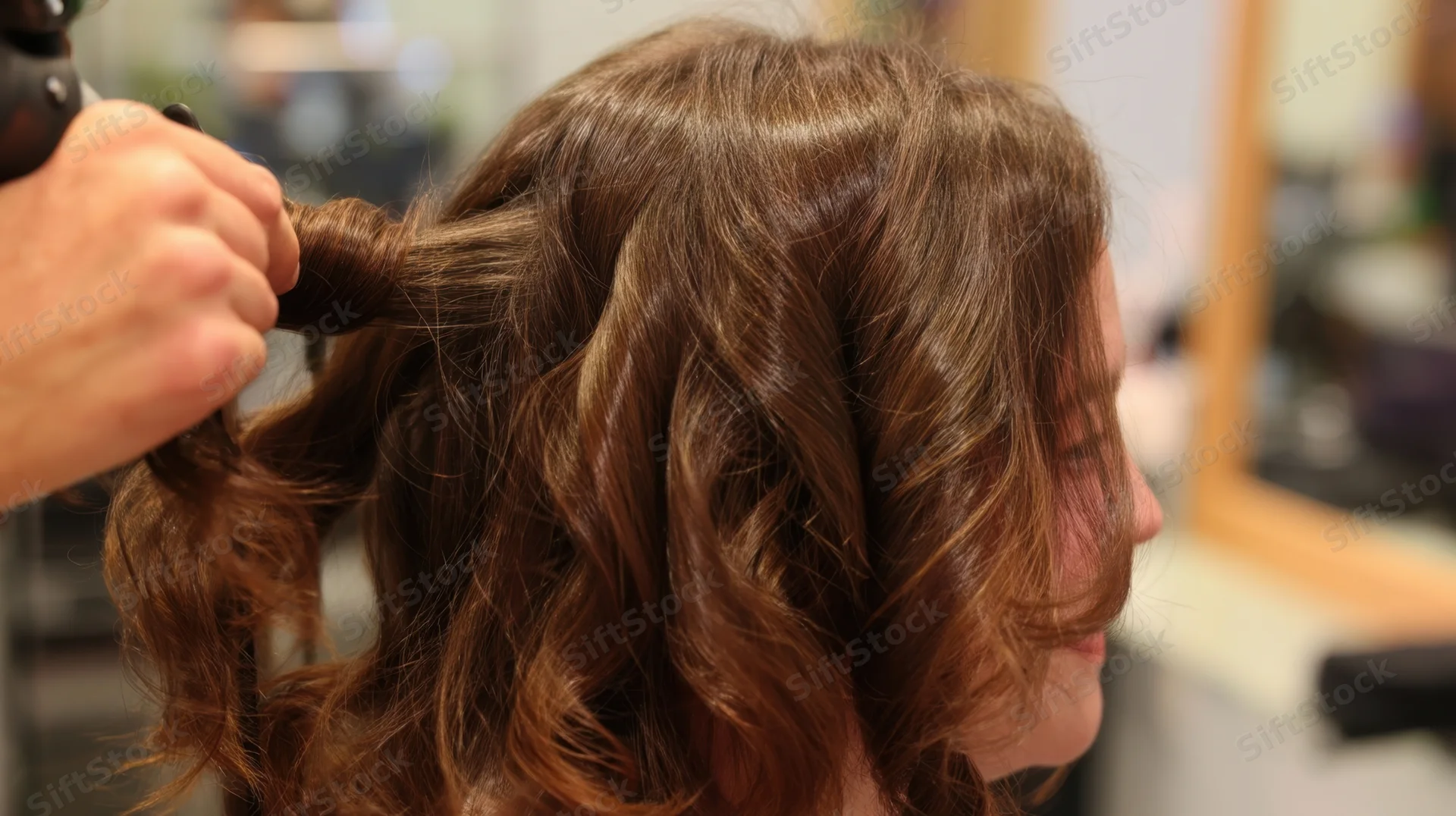Woman receiving hair styling with curling iron in salon