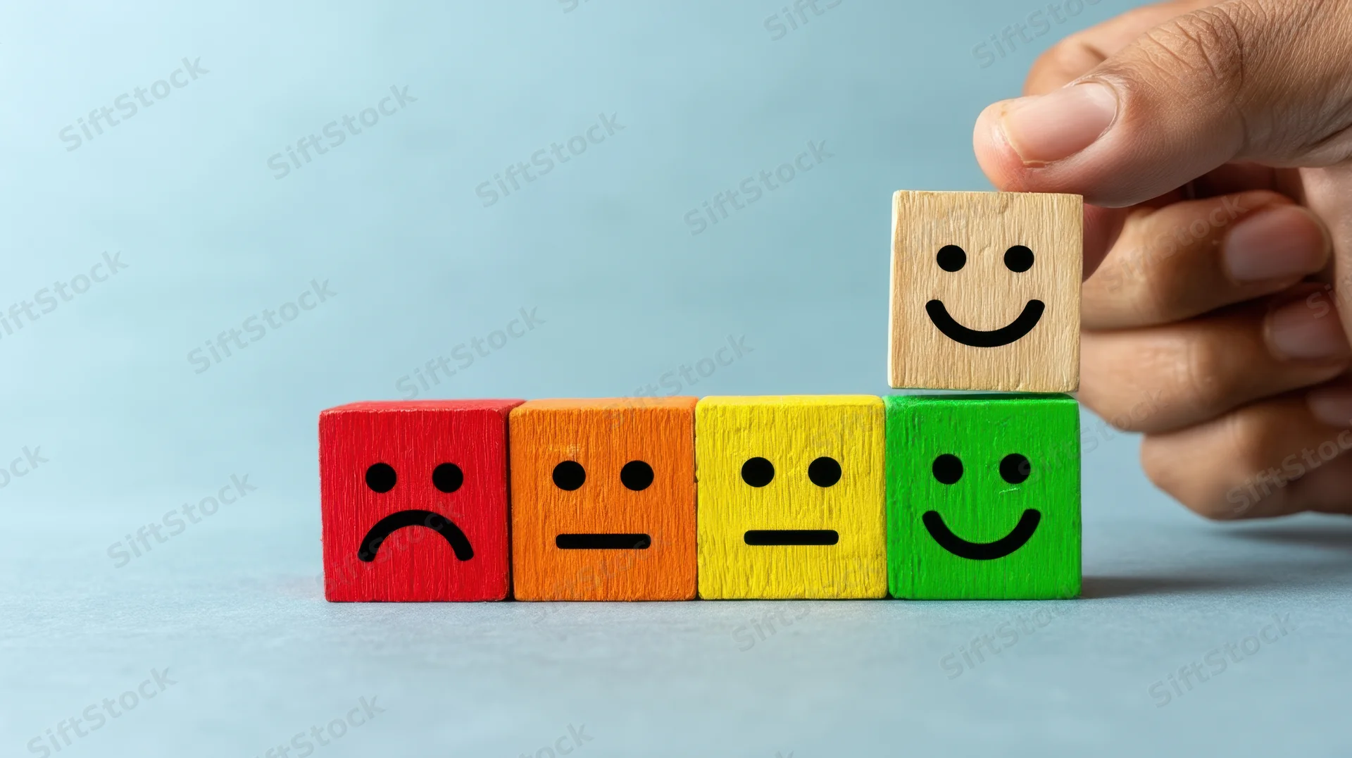 Hand placing a smiling wooden block on top of a row of colored blocks with facial expressions indicating feedback levels