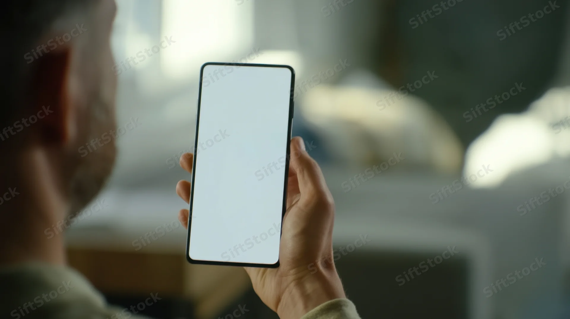 Man holding smartphone with blank white screen indoors