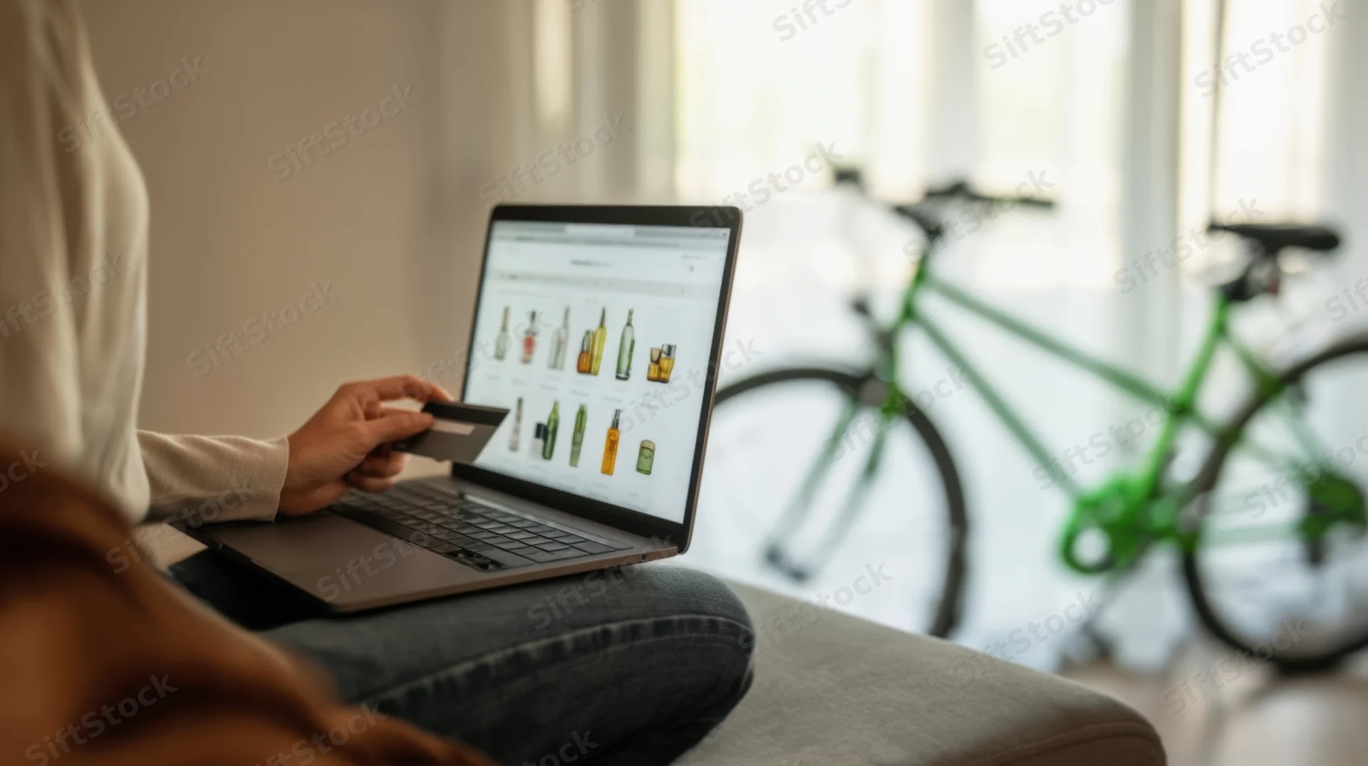 Woman sitting on sofa using laptop for online shopping with credit card, green bicycle visible in background