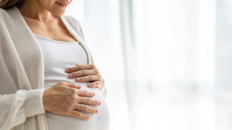 Pregnant woman cradling her belly indoors by a window
