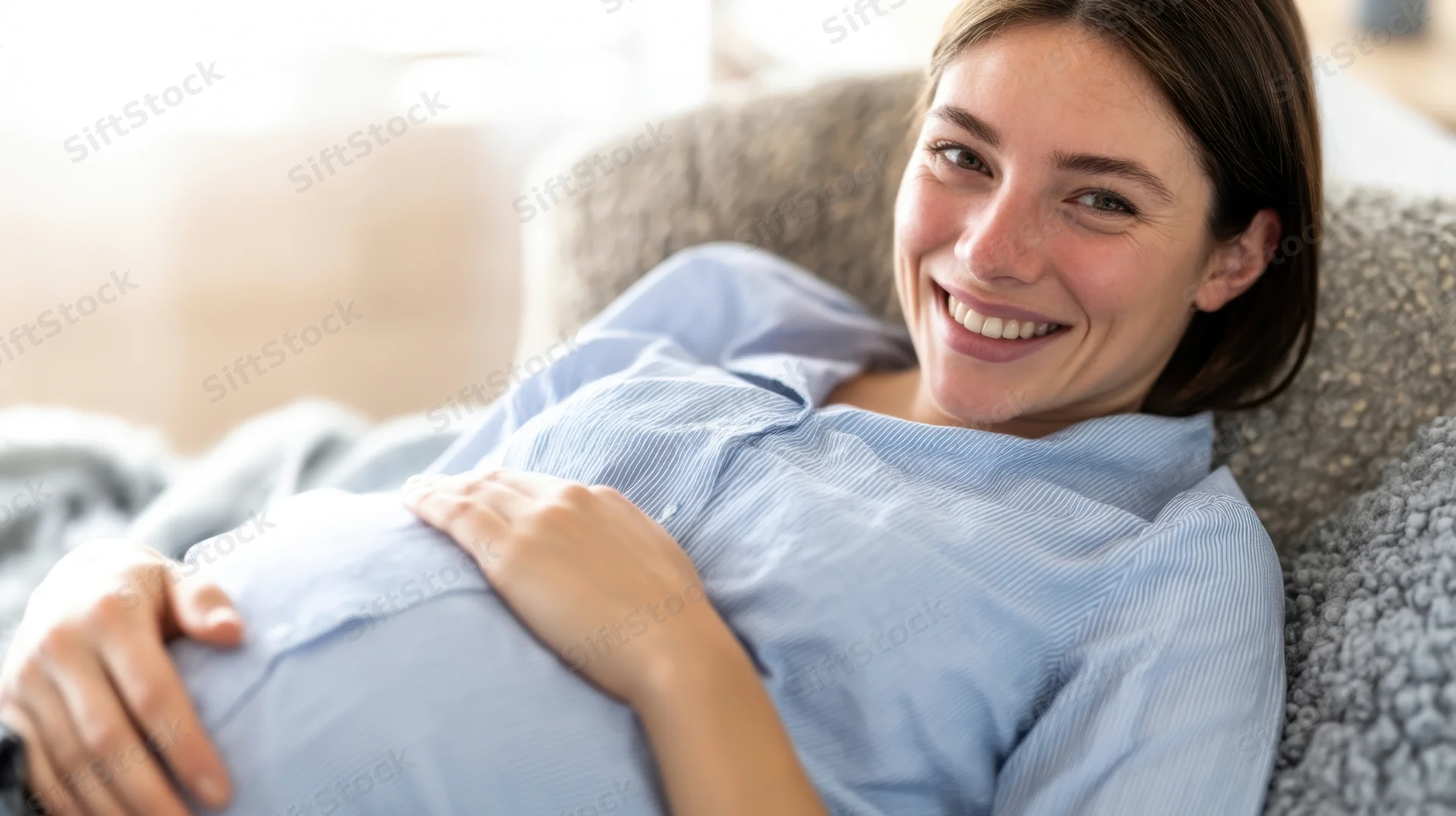 Pregnant woman smiling while resting on a couch with hands on her belly