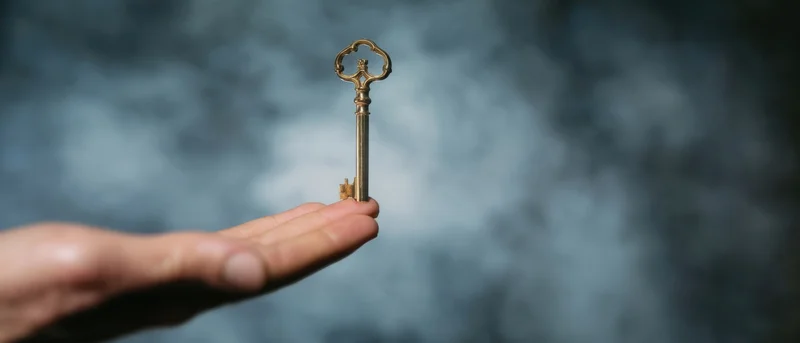 Hand holding a vintage brass key against a blurred dark background