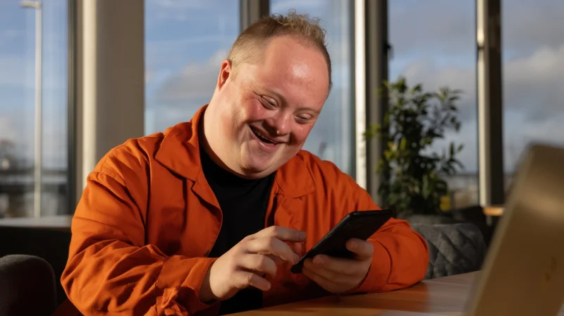 Young man smiling while using smartphone at office desk near window