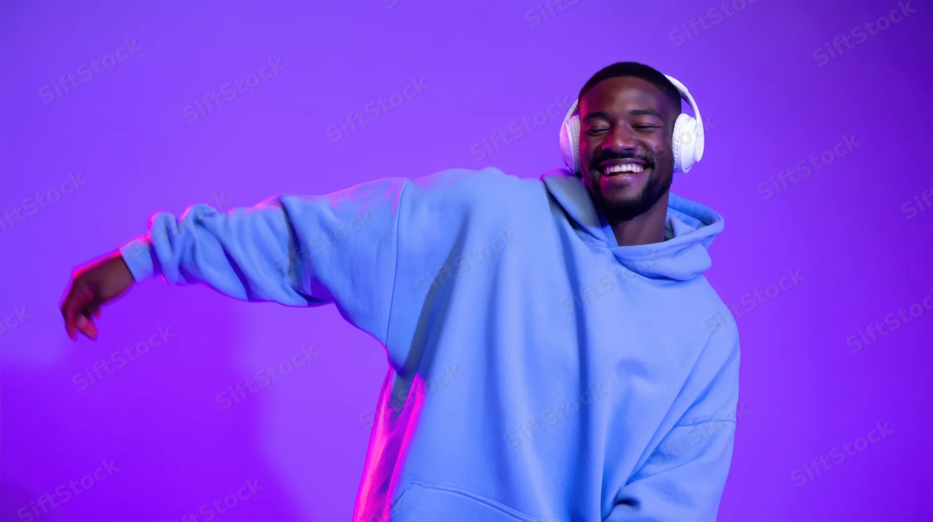 Young man smiling and dancing with headphones in a purple neon studio