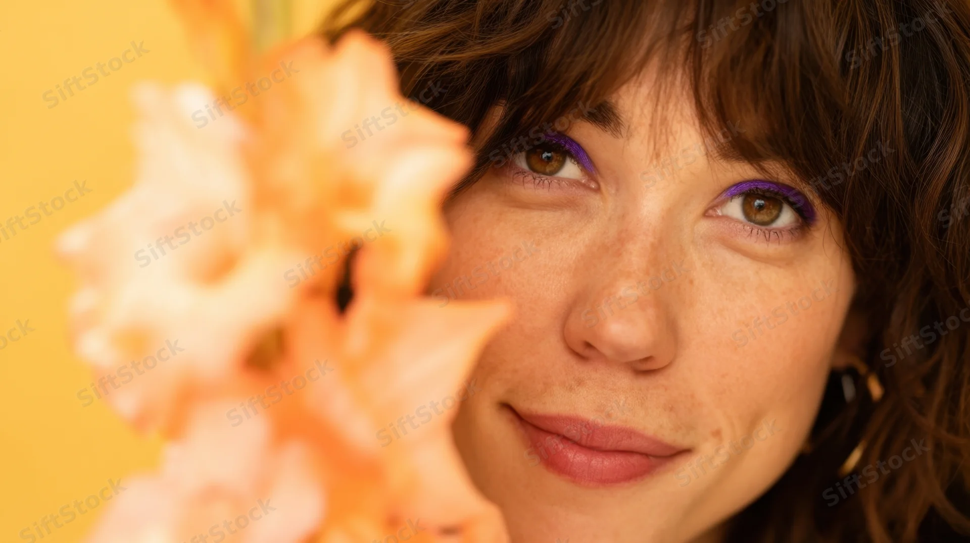 Young woman smiling with peach flower near her face against yellow background