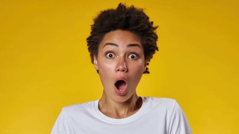 Young woman with wide eyes and open mouth showing surprise against yellow background
