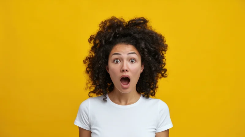 Young woman with curly hair showing surprised expression against yellow background