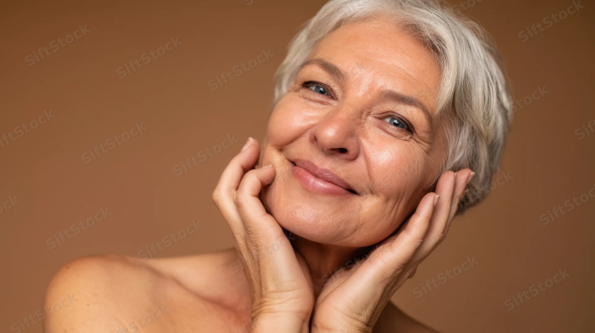 Senior woman smiling with hands on her face in studio portrait