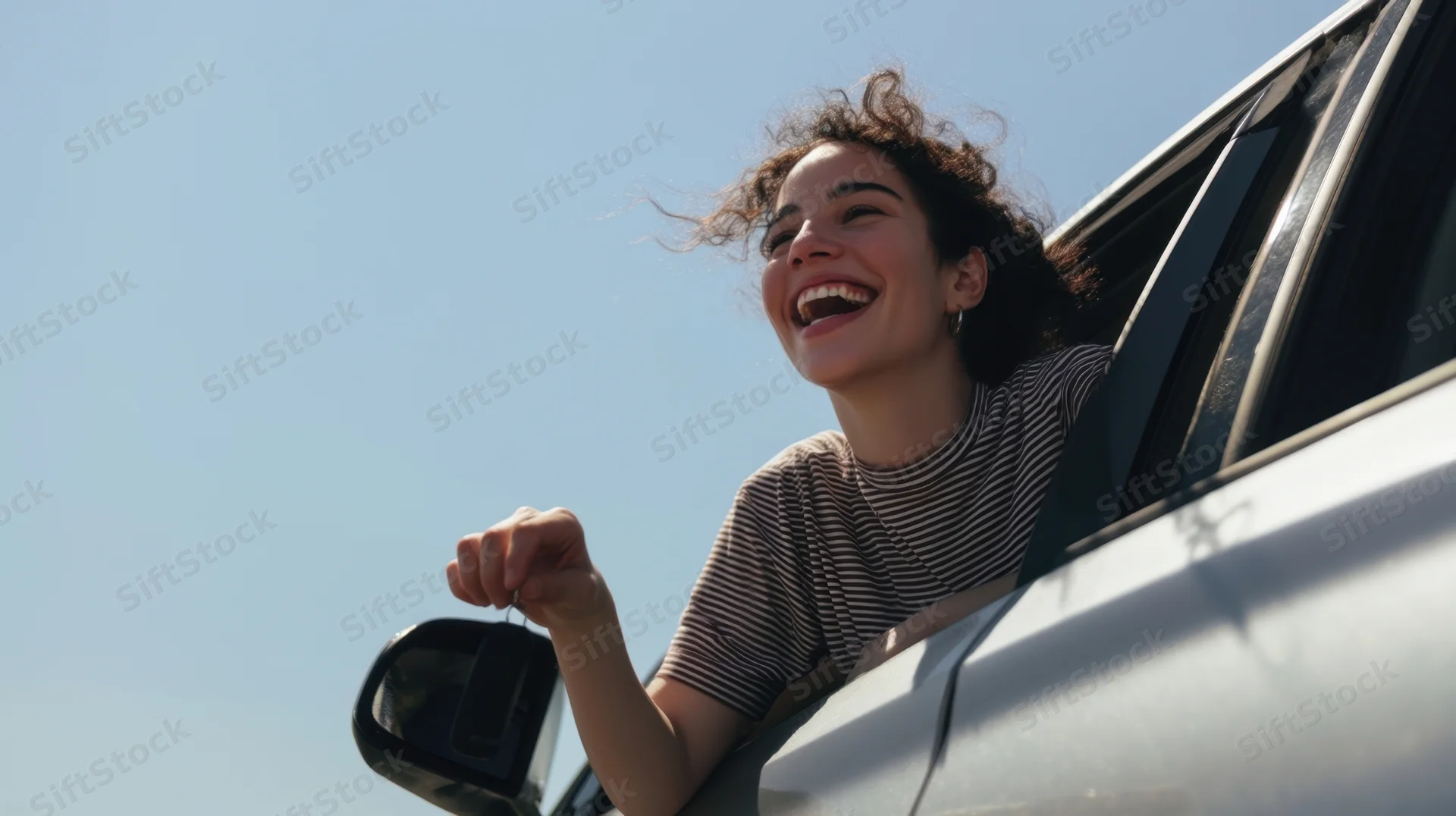 Young woman laughing with head out of car window on a sunny day