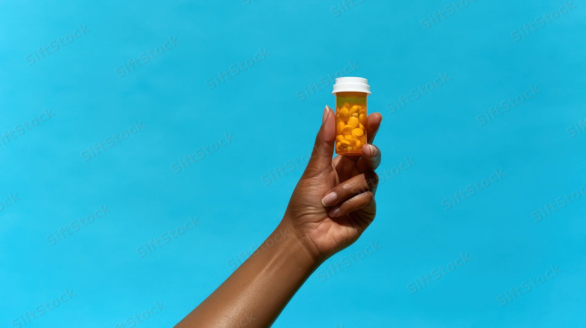 Hand holding a prescription pill bottle against a blue background