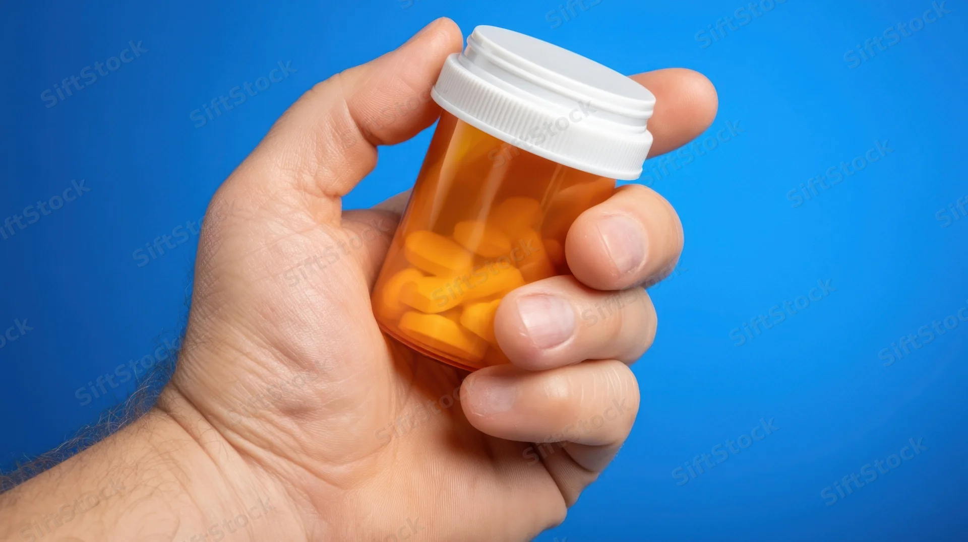 Hand holding a prescription pill bottle against blue background