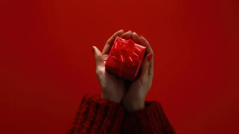 Woman's hands holding a small red gift box with ribbon against a red background