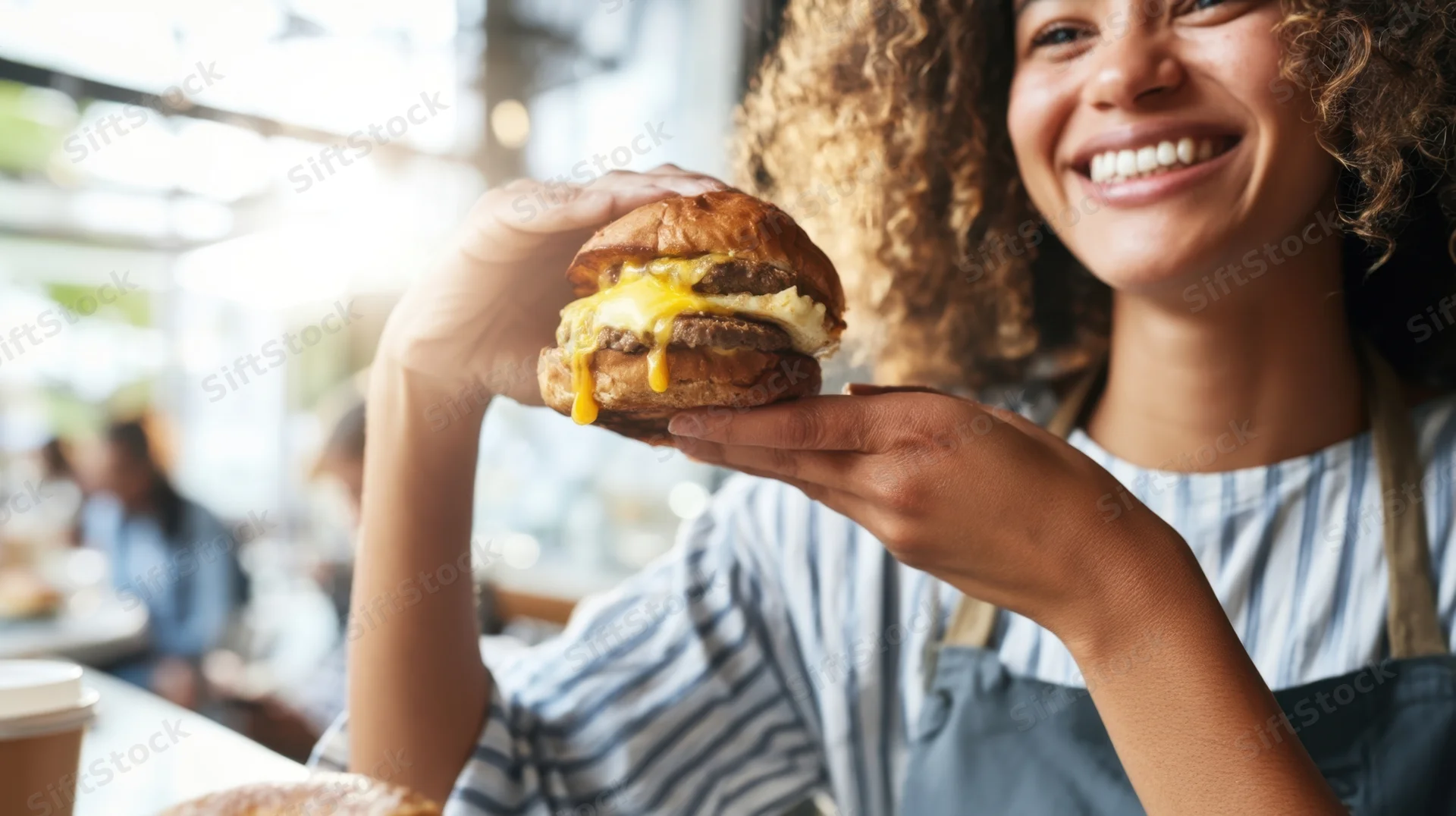 Woman holding a cheeseburger with melted cheese dripping, smiling in a restaurant