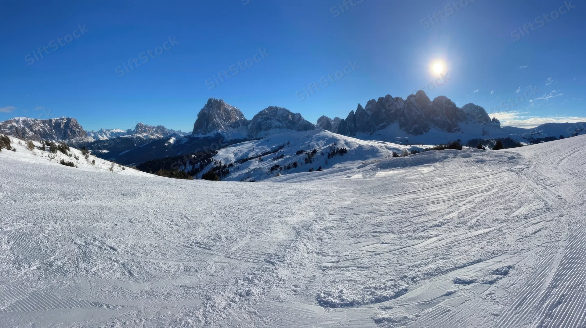 Snow-covered mountain range under bright sun with ski tracks on slope