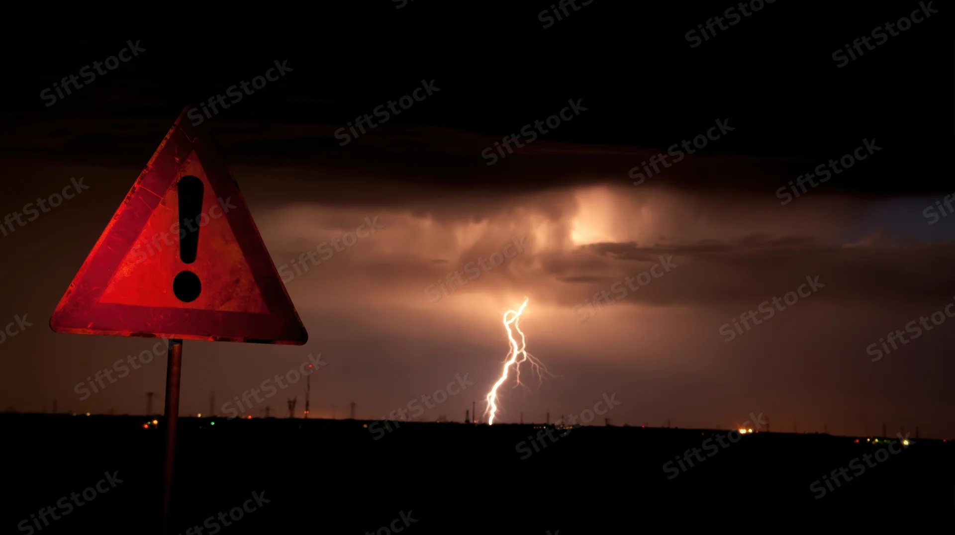 Red triangular warning sign in a stormy night sky with lightning striking in the distance