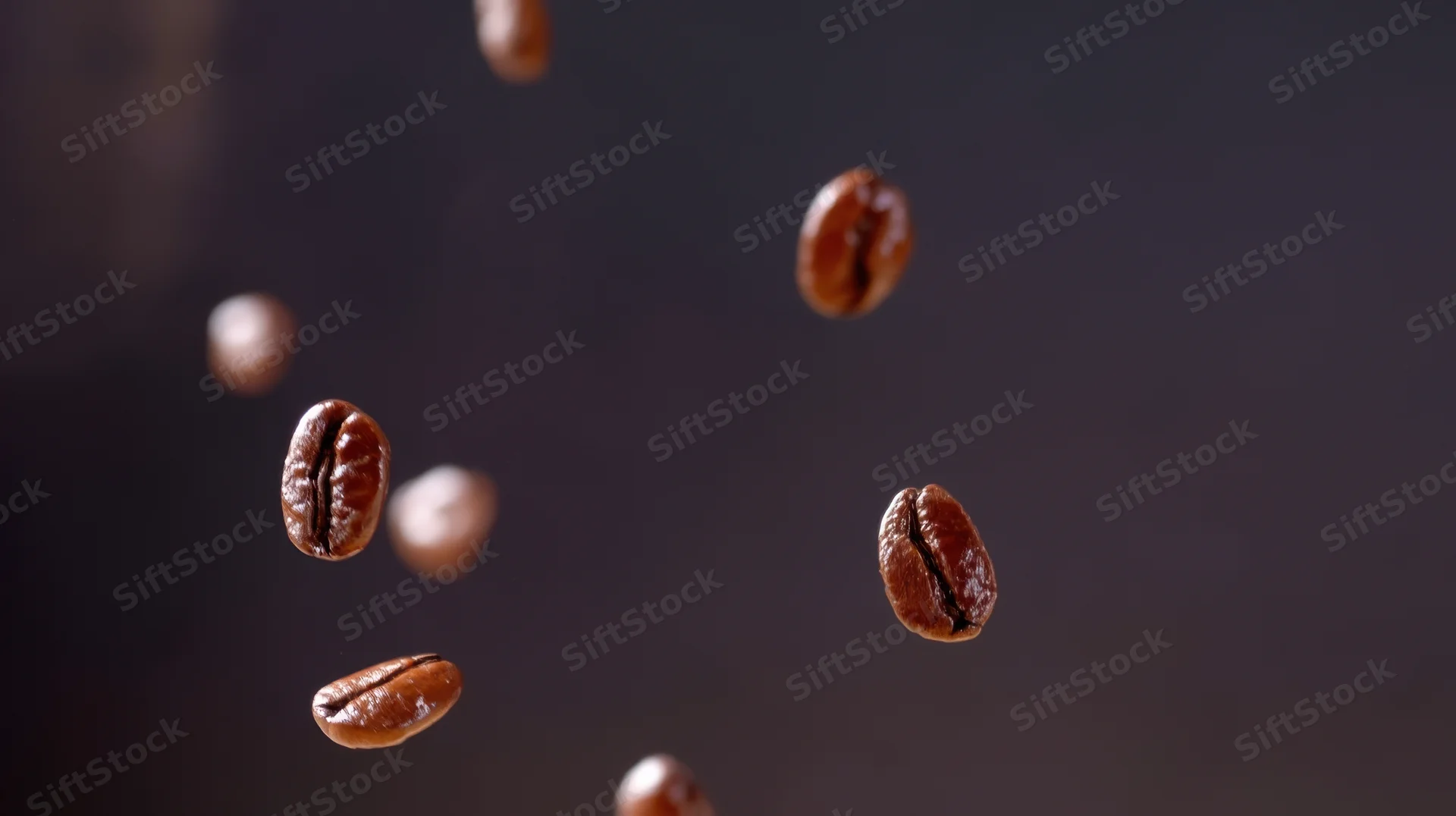 Roasted coffee beans falling in midair against a dark background