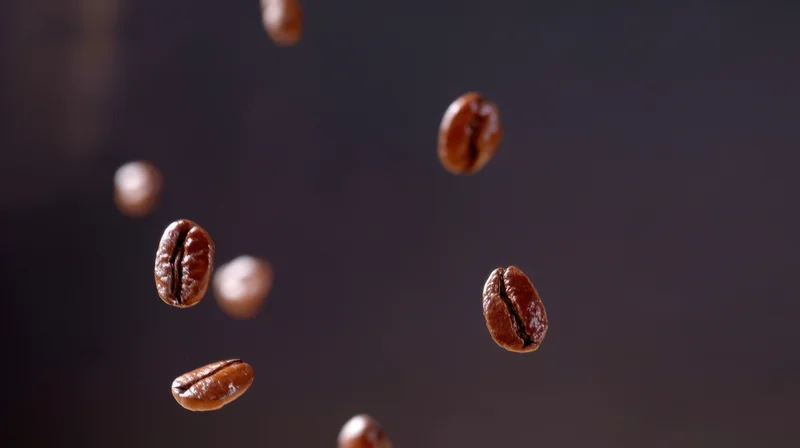 Roasted coffee beans falling in midair against a dark background