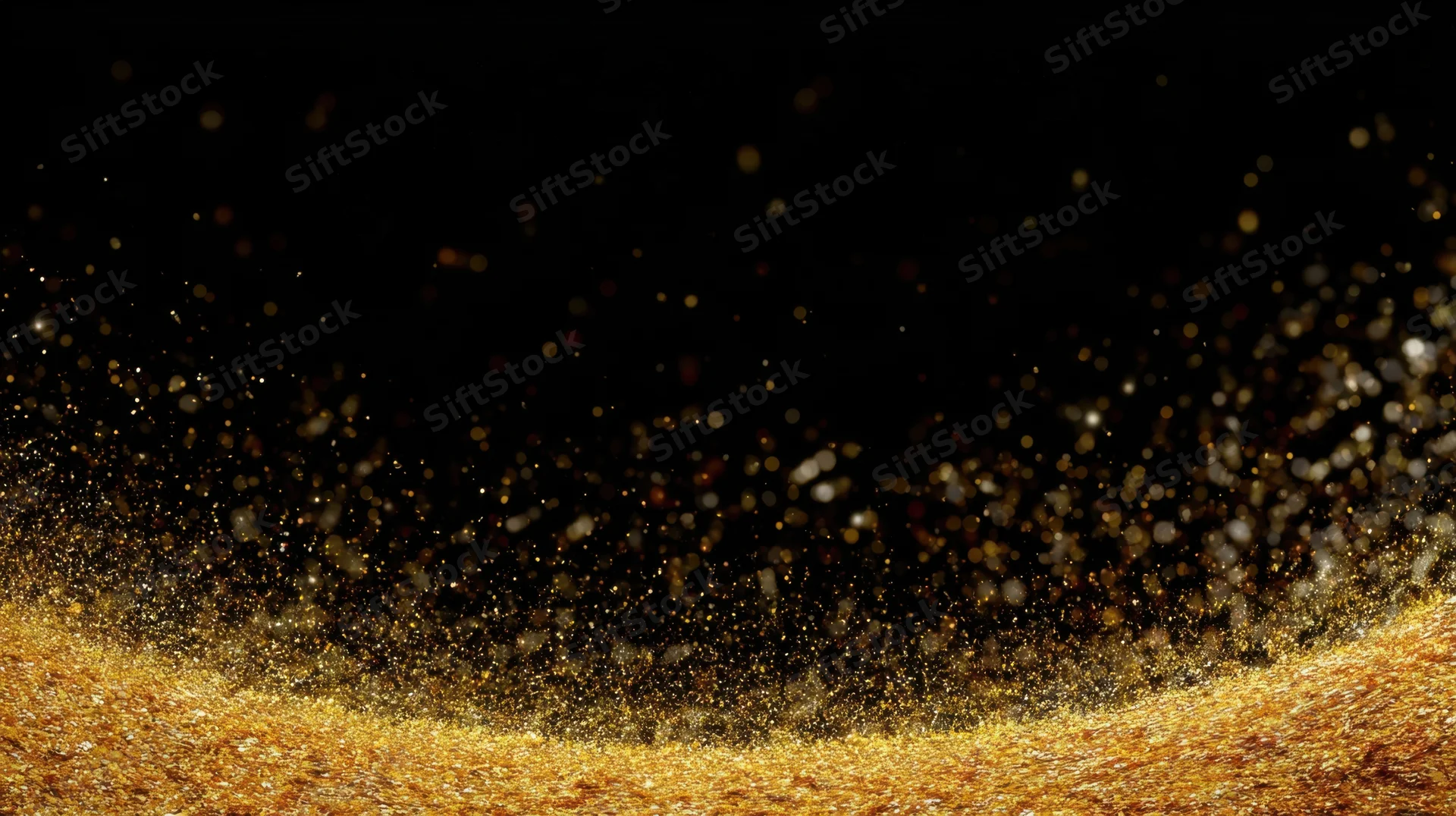 Golden glitter particles floating above a shimmering surface against a black background