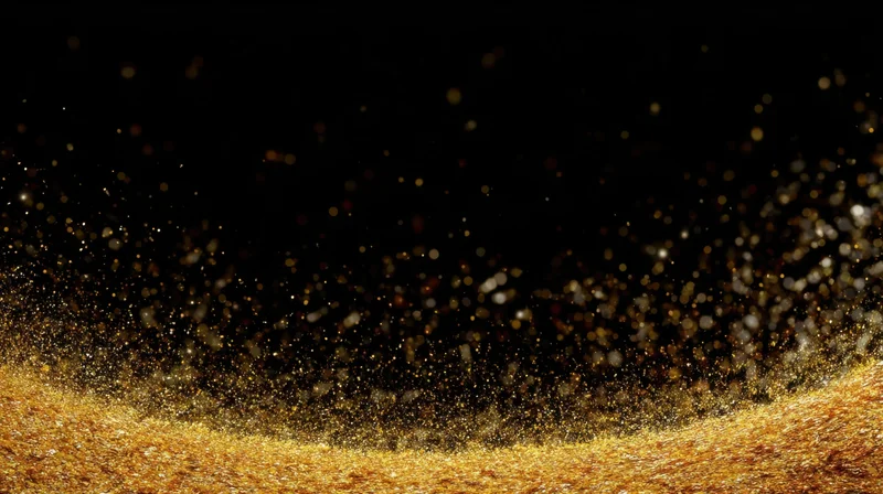 Golden glitter particles floating above a shimmering surface against a black background