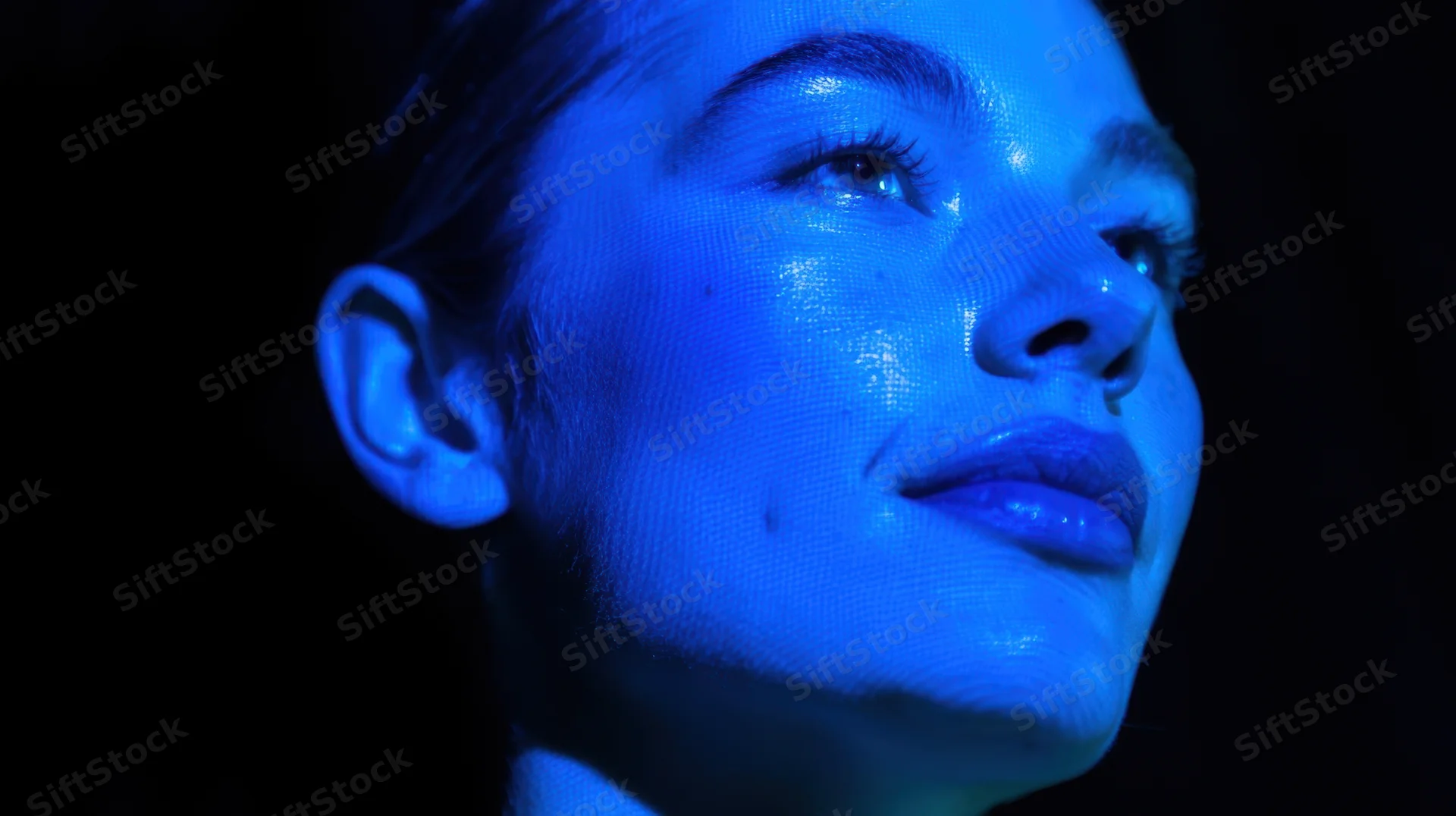 Close-up of a woman's face illuminated by blue light in a dark setting