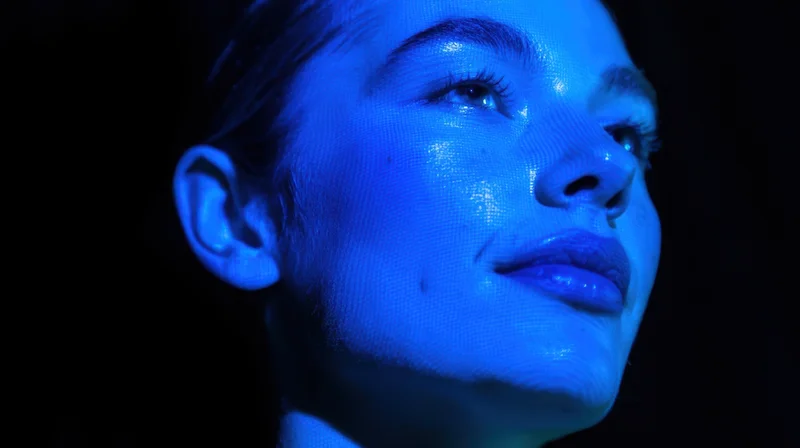 Close-up of a woman's face illuminated by blue light in a dark setting
