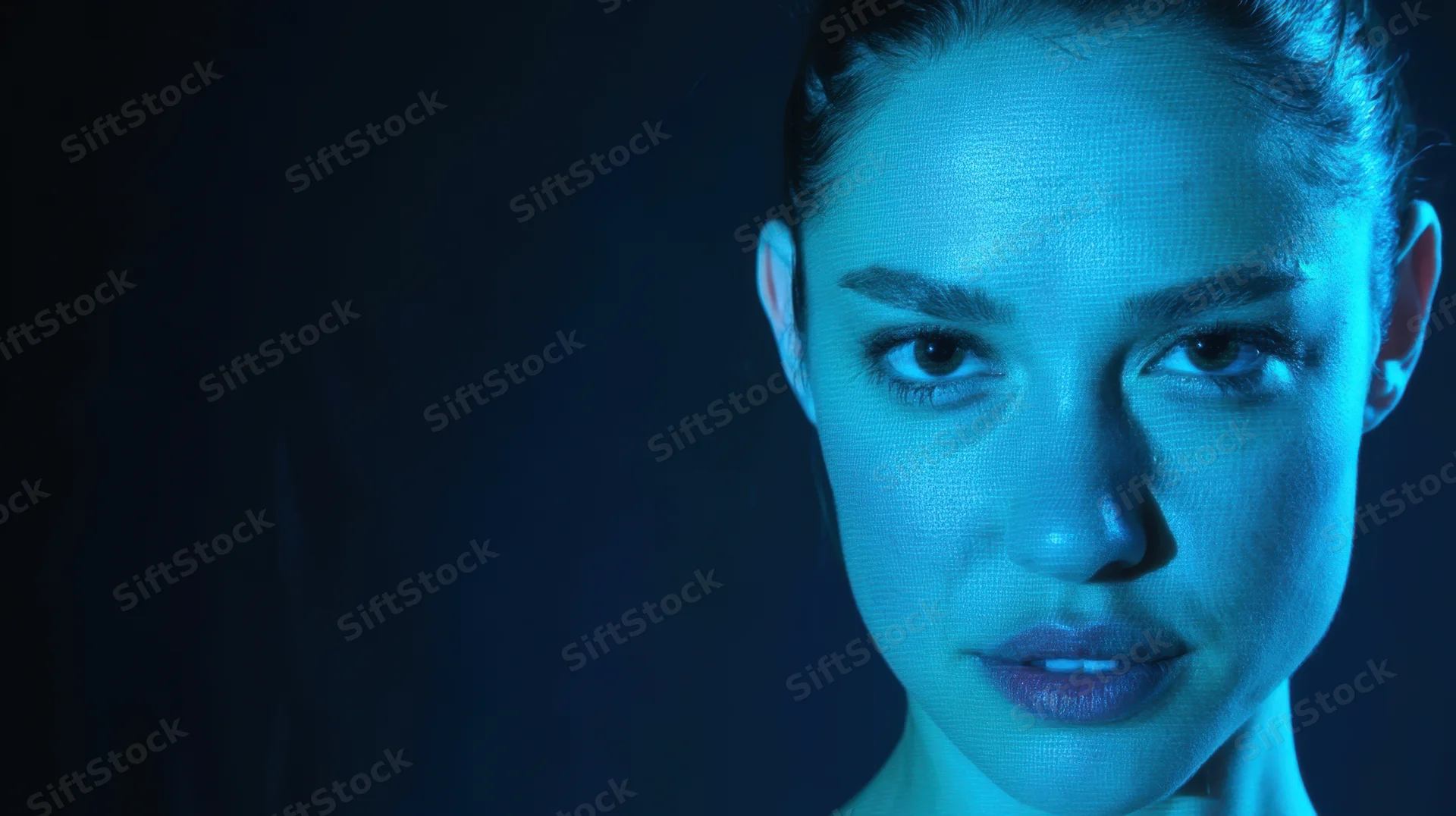 Close-up of a woman's face illuminated by blue digital light against a dark background