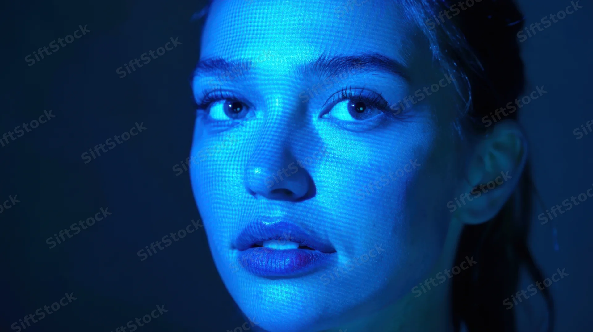 Close-up of a woman's face illuminated by blue digital grid light against dark background