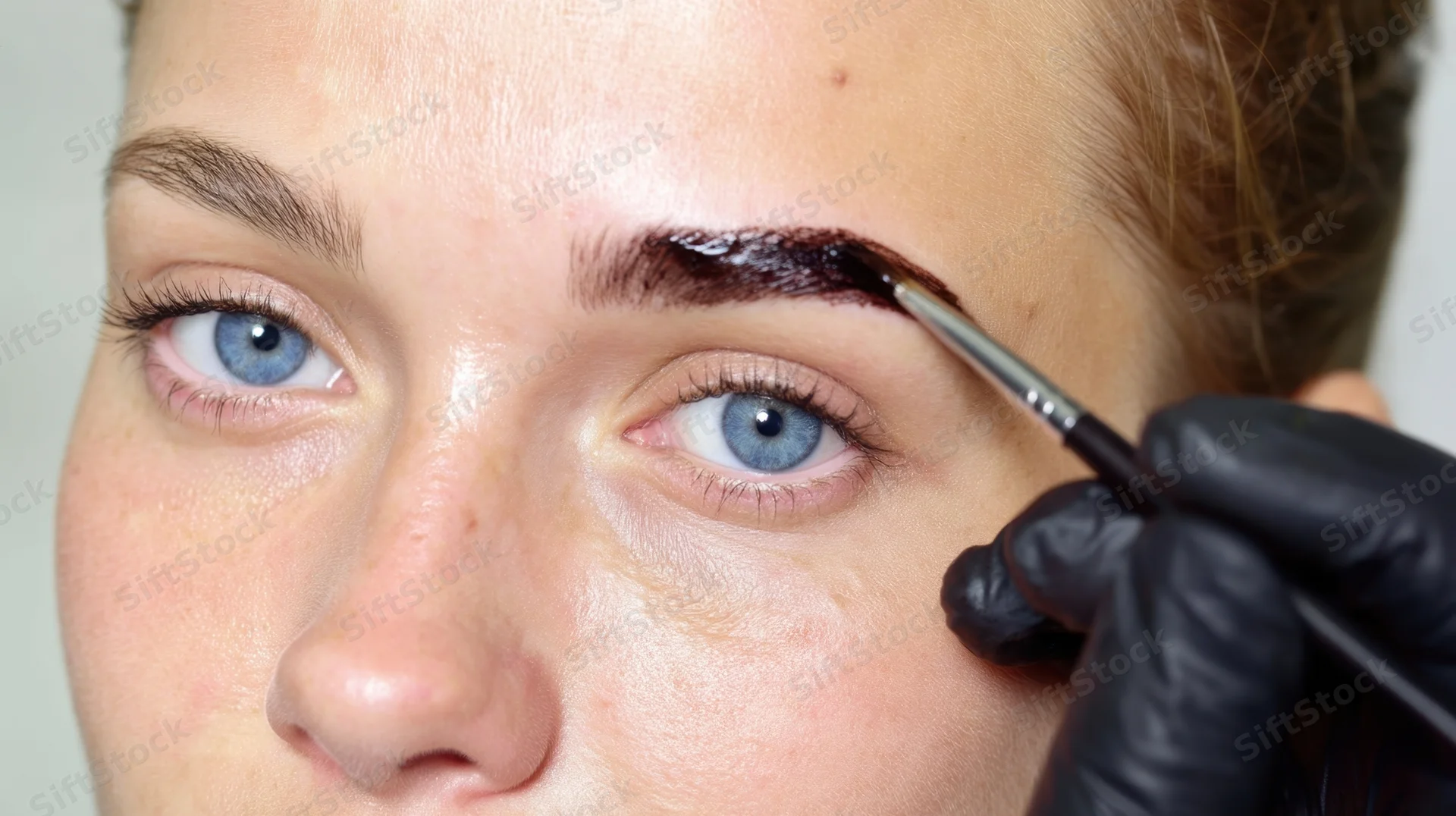 Woman receiving eyebrow tint application with precision brush in salon setting