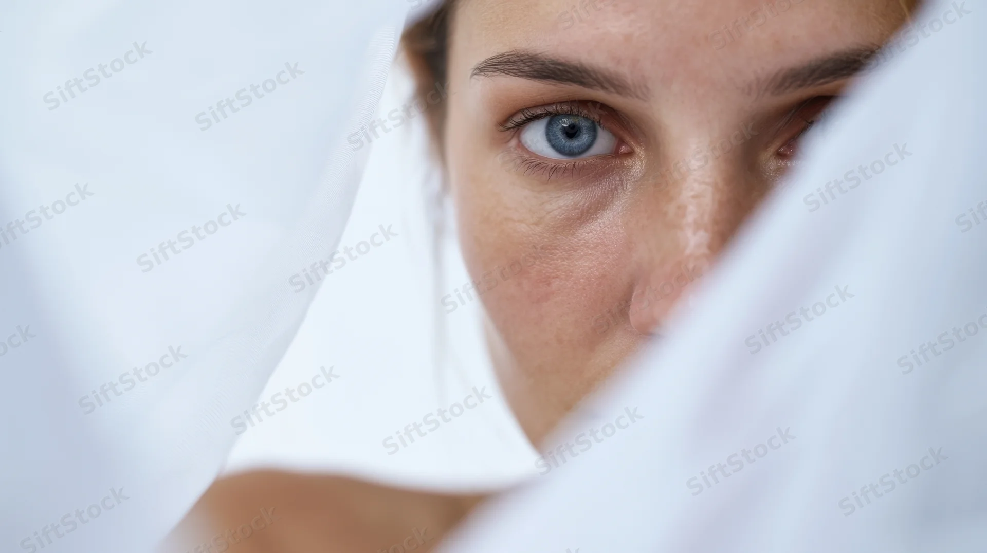 Woman peeking through white fabric with blue eyes in close-up view
