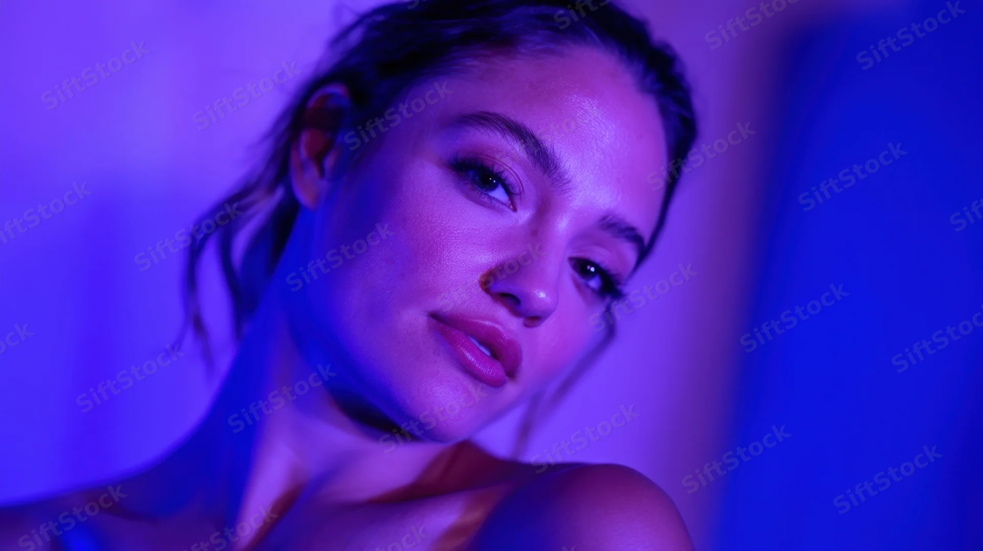 Woman in closeup portrait with blue and purple neon lighting, soft gaze, smooth skin, visible shoulder and neck