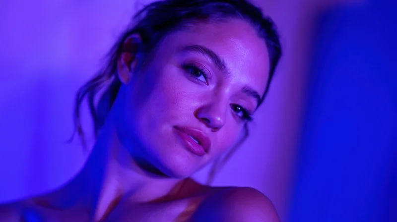Woman in closeup portrait with blue and purple neon lighting, soft gaze, smooth skin, visible shoulder and neck
