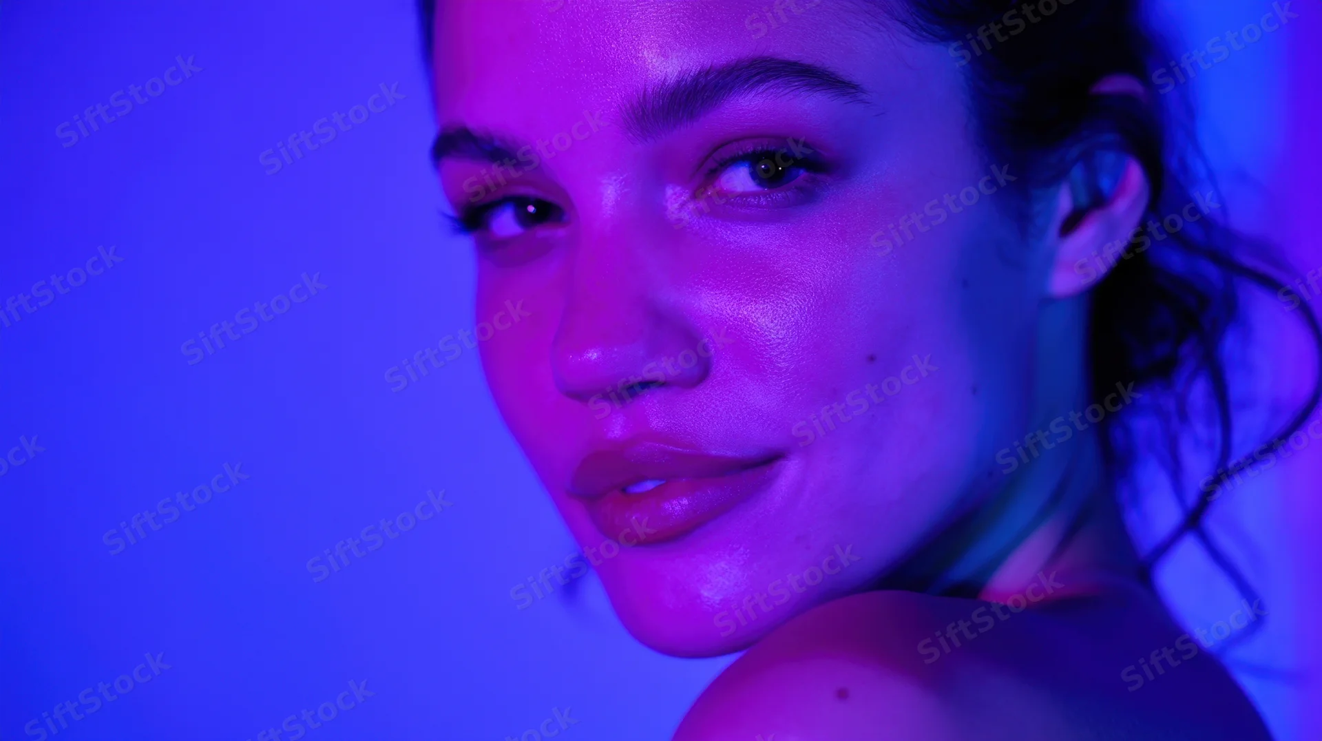 Woman with glowing skin under purple and blue neon lights in studio portrait