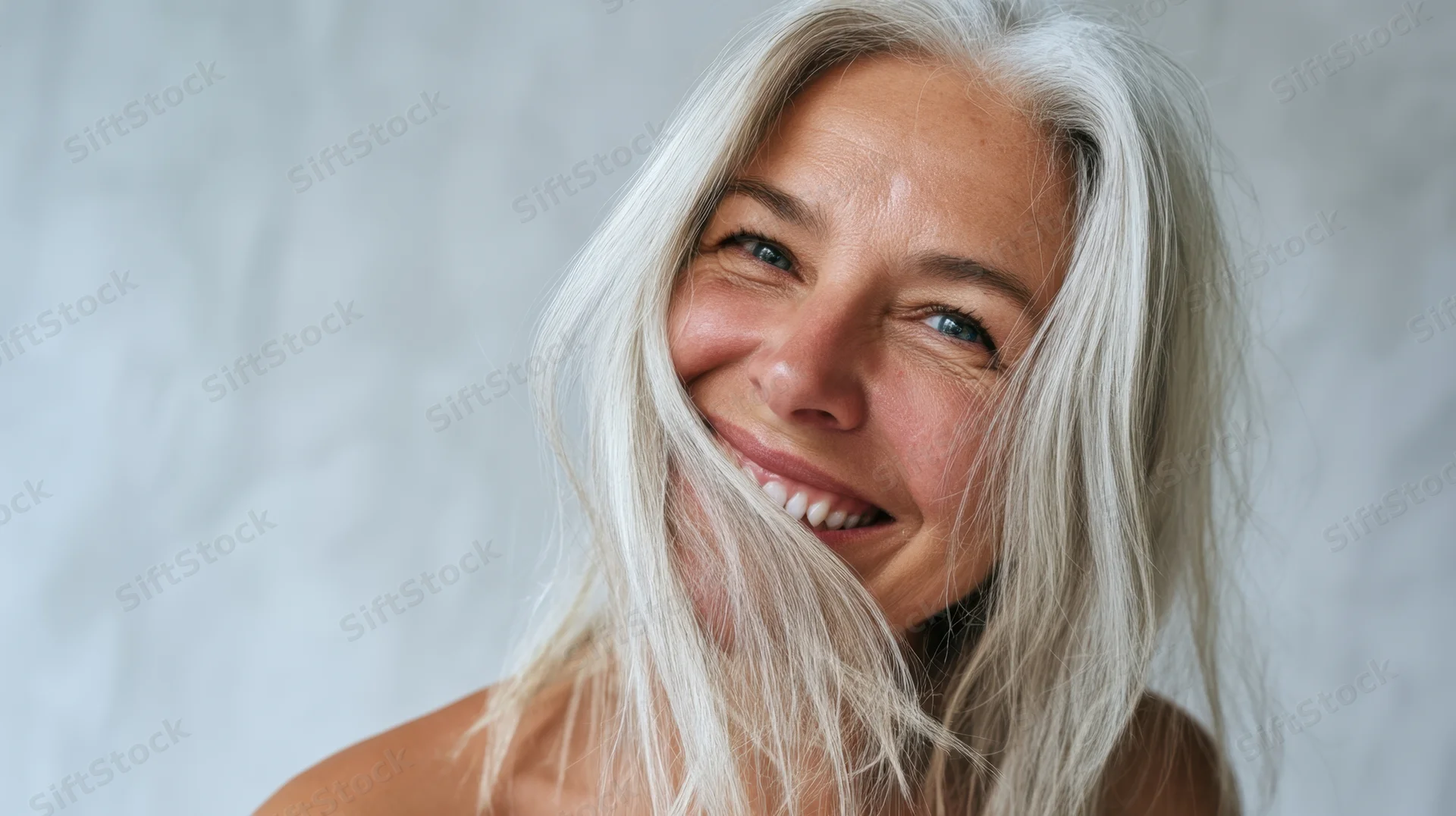 Smiling senior woman with white hair and blue eyes in closeup portrait against soft gray background