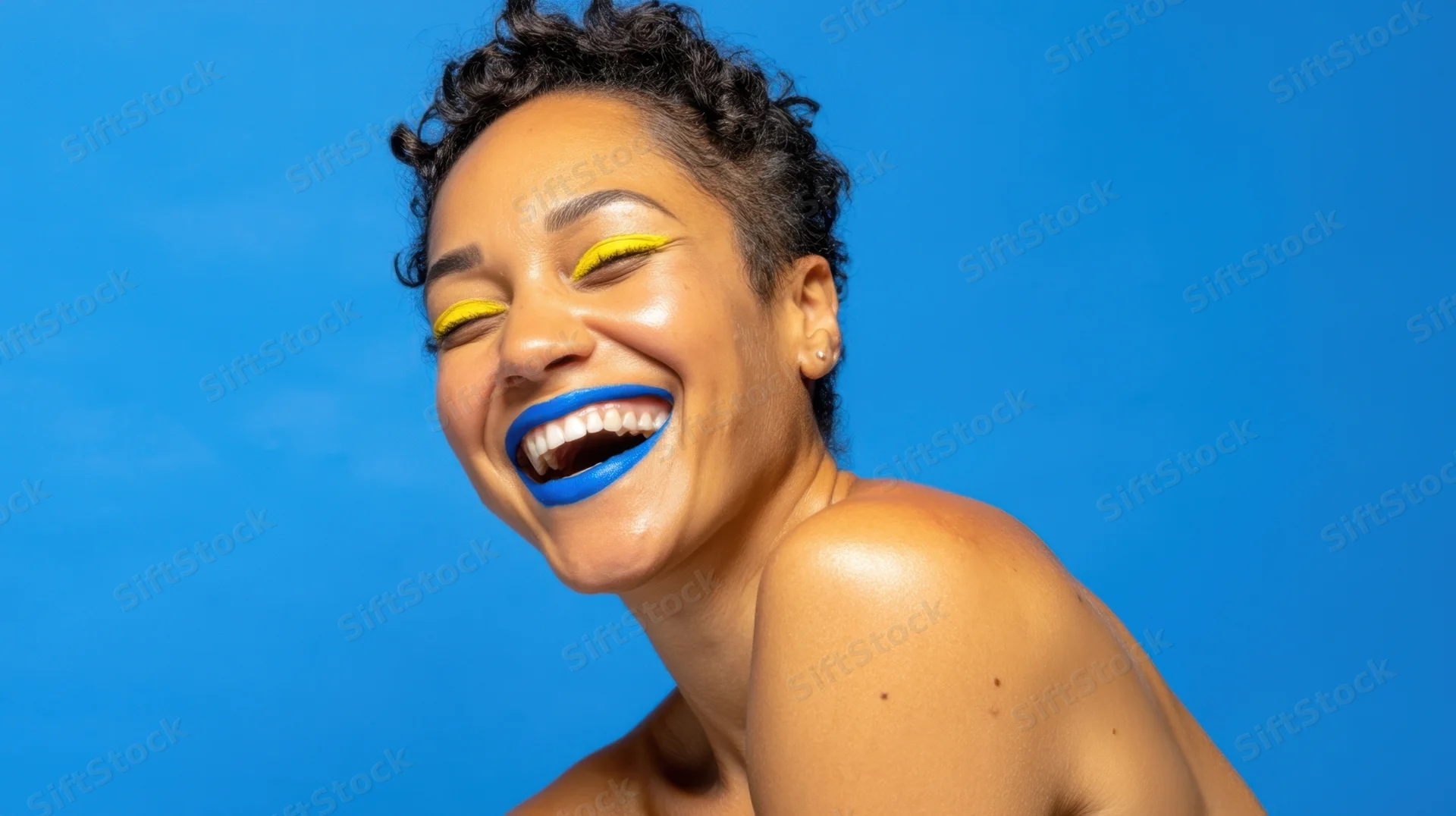 Woman laughing with bright blue lipstick and yellow eyeliner against a blue background